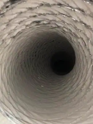 A close-up view looking down the inside of a metallic ventilation duct, showing spiral ridges along its interior and a dark center at the far end, highlights the importance of air duct services New Jersey.