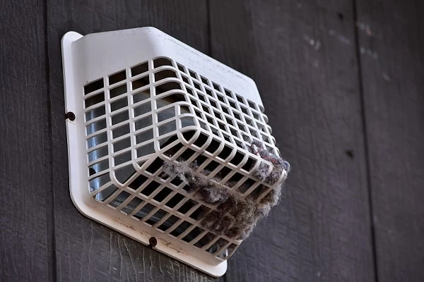 A white outdoor vent cover on a dark wall is clogged with lint and debris, highlighting the importance of regular dryer vent cleaning New Jersey to maintain safety and efficiency.