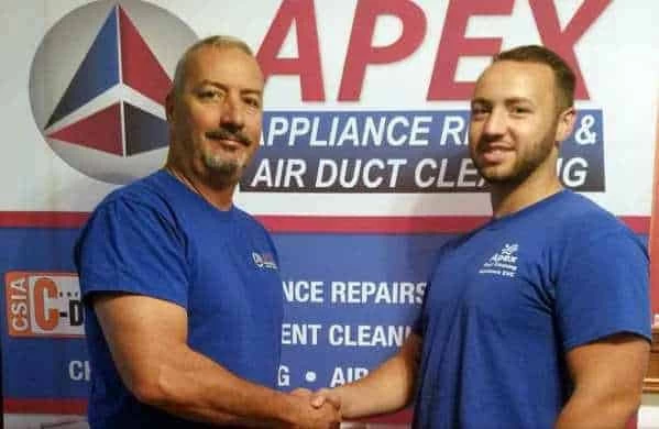 Two men wearing blue shirts shake hands and smile in front of a sign that reads "APEX Appliance Repair & Air Duct Cleaning," highlighting trusted air duct services New Jersey residents rely on.