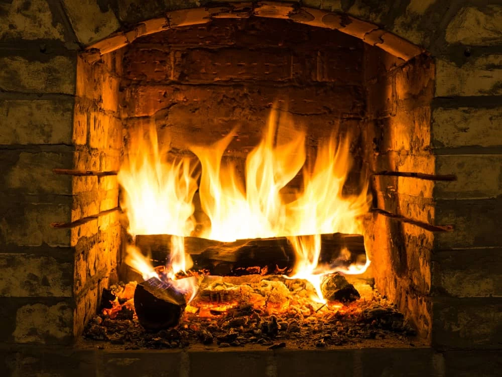 A cozy fire burns brightly in a rustic brick fireplace, with orange and yellow flames rising from logs and glowing embers beneath&mdash;perfect warmth after expert air duct services New Jersey has to offer.