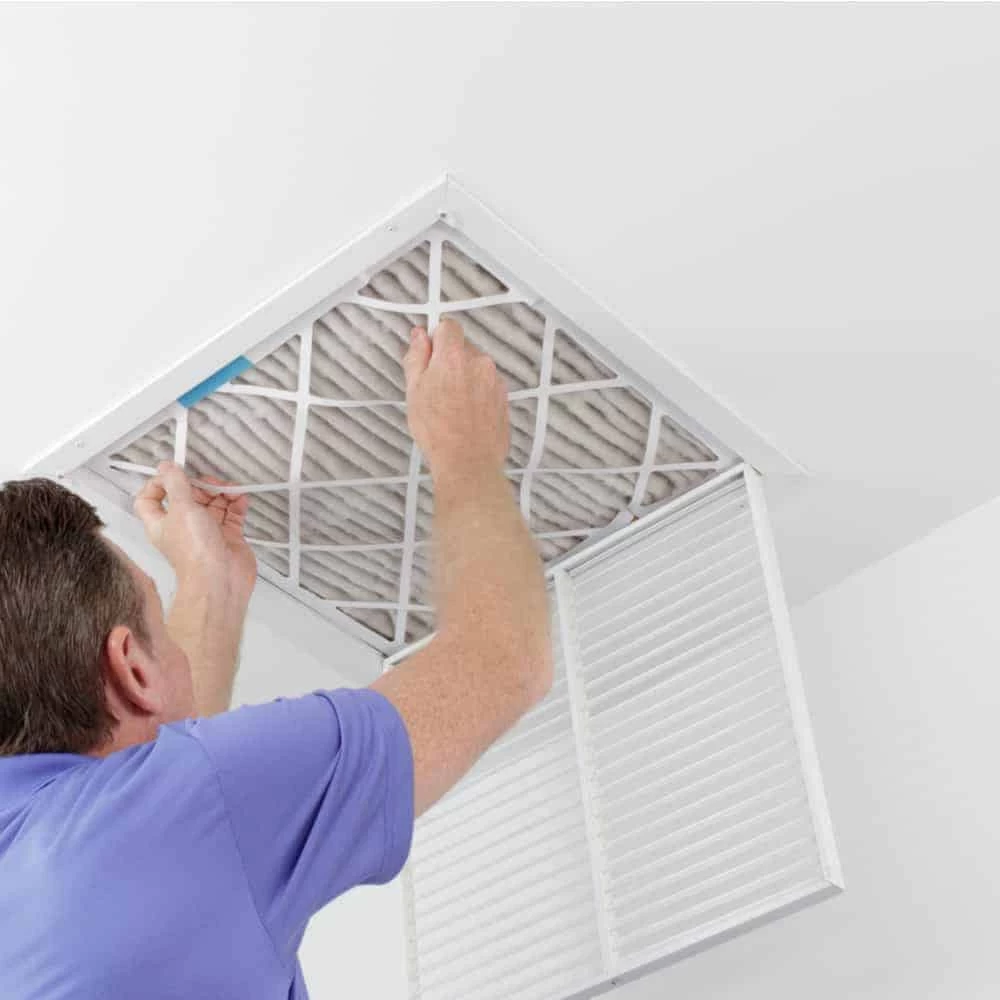 A person in a blue shirt is removing or installing an air filter in a ceiling vent, with the vent cover open&mdash;demonstrating professional air duct services New Jersey residents can rely on.