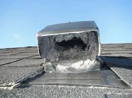 A close-up of a roof vent clogged with lint and debris on a shingled roof under a blue sky&mdash;a clear reminder of the importance of regular dryer vent cleaning New Jersey homeowners should consider.
