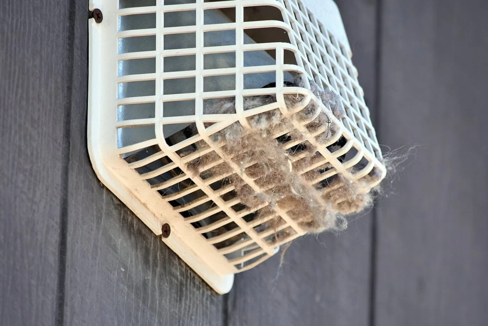 A white outdoor vent cover attached to a dark wall is clogged with lint and dust, restricting airflow&mdash;an issue easily resolved with professional dryer vent cleaning New Jersey.