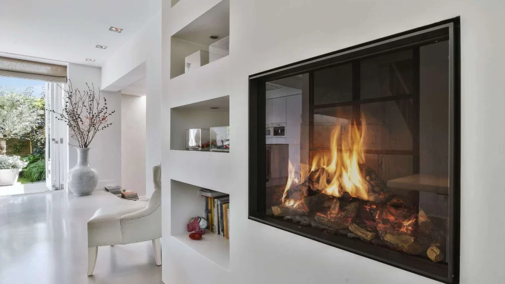 Modern, bright living room with a glass-enclosed fireplace, white built-in shelves, and sunlight streaming in from an open door leading to a garden&mdash;enjoy comfort year-round with expert air duct services New Jersey.