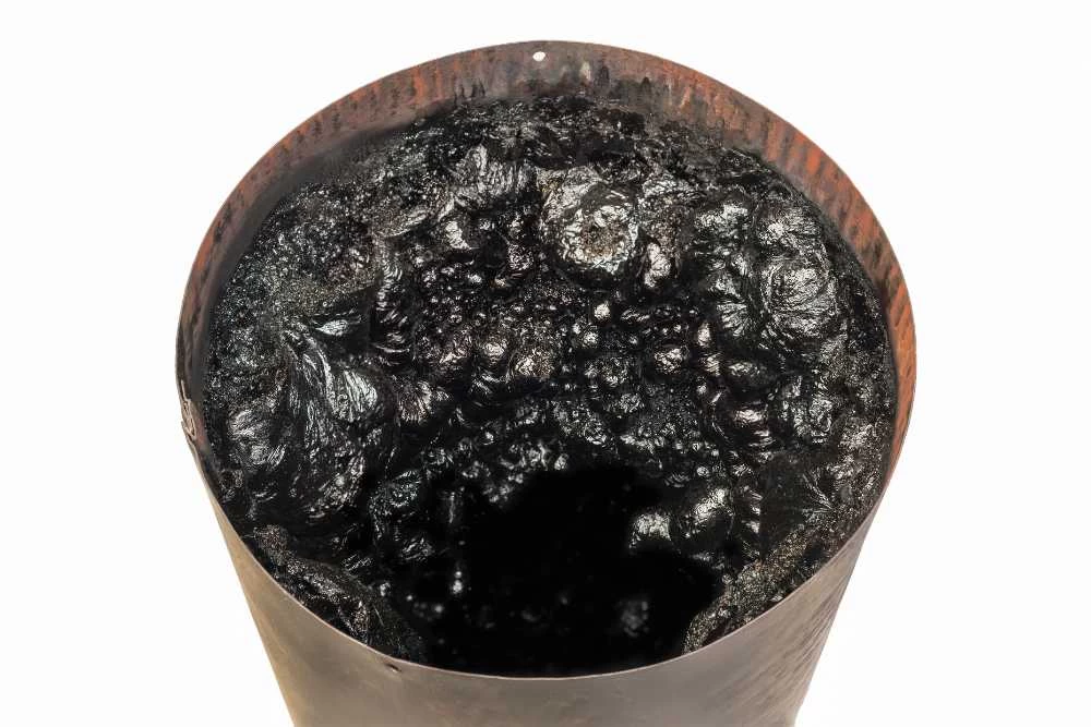 A close-up view of a rusty, cylindrical metal container filled with thick, black, tar-like substance, seen from above against a white background&mdash;reminiscent of residue often found during air duct services New Jersey.