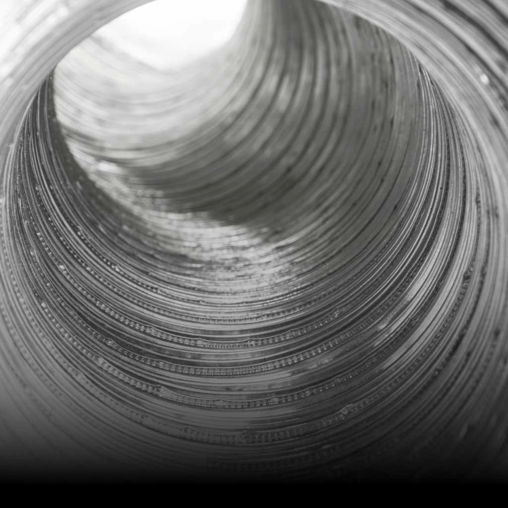 Close-up view of the inside of a metallic spiral or coil, resembling the interior of dryer vents often seen in dryer vent cleaning New Jersey services. The black and white image accentuates the metal&rsquo;s texture, shine, and tunnel-like effect.