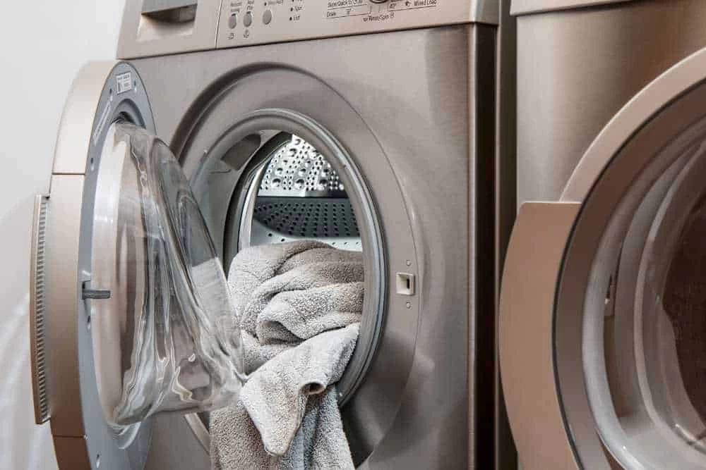 A front-loading washing machine with the door open reveals light gray towels inside the drum, while a matching dryer sits beside it&mdash;a perfect setup for those seeking dryer vent cleaning New Jersey services.