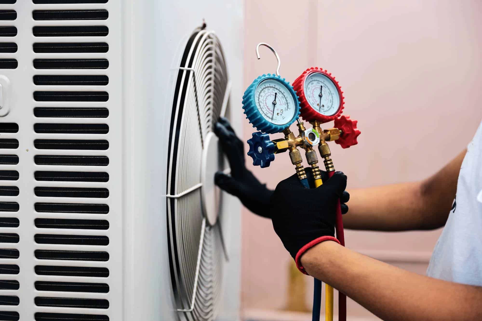 A person wearing black gloves uses a manifold gauge set to check or service an outdoor air conditioning unit, a common part of air duct services New Jersey professionals offer for better home efficiency.