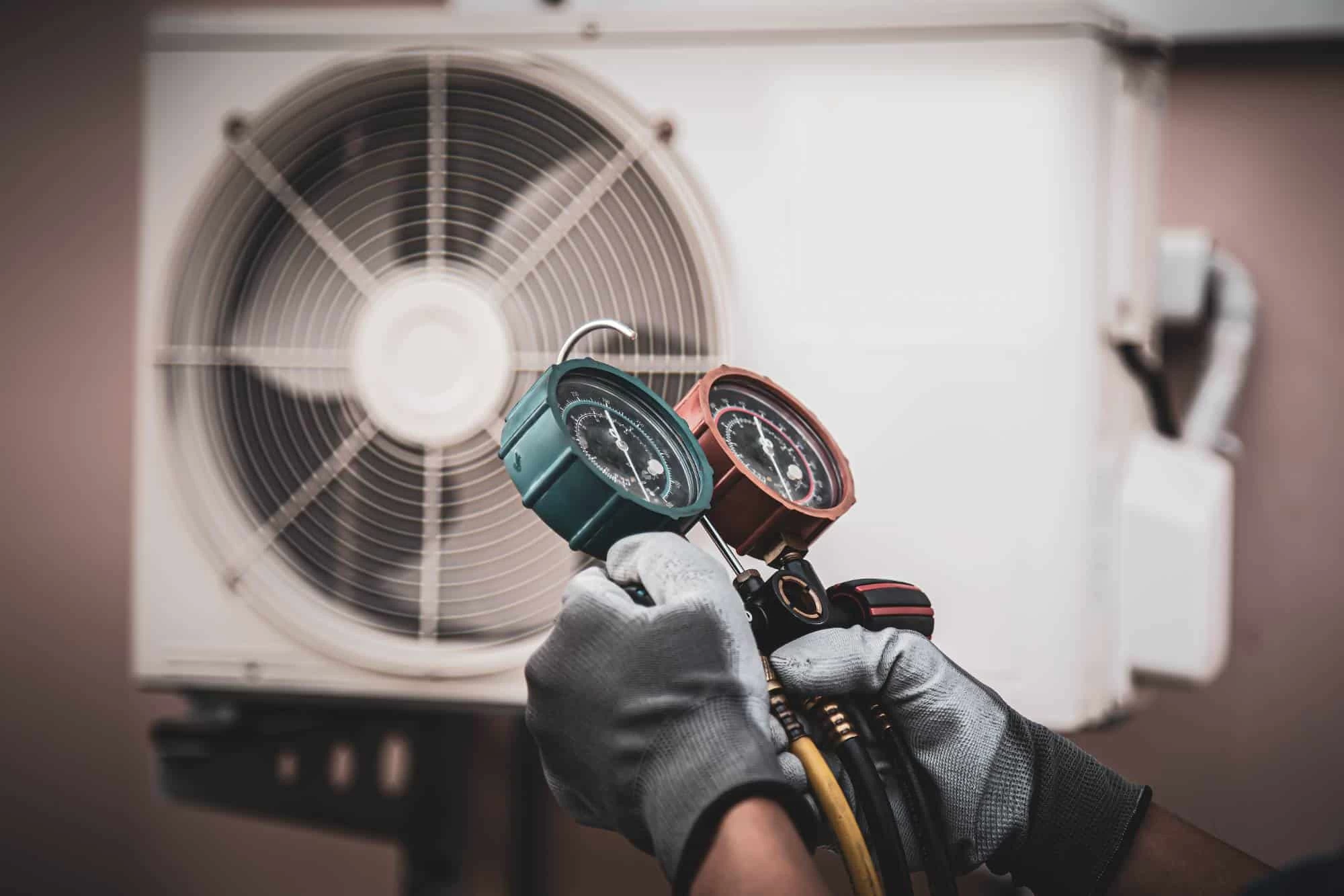 A technician wearing gloves uses a gauge manifold to check the refrigerant level of an outdoor air conditioning unit, ensuring efficient cooling and complementing our professional air duct services New Jersey.