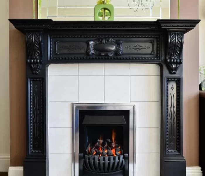 A decorative black fireplace with a white tile surround and a small fire inside. The mantel holds tall black candles, a green vase with yellow flowers, and sits below a large mirror&mdash;perfect for cozy nights or after air duct services New Jersey.